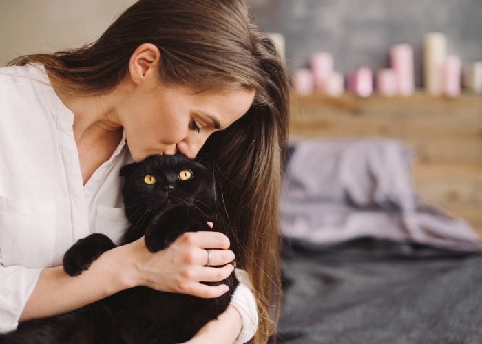 Image of a woman kissing a black cat. 